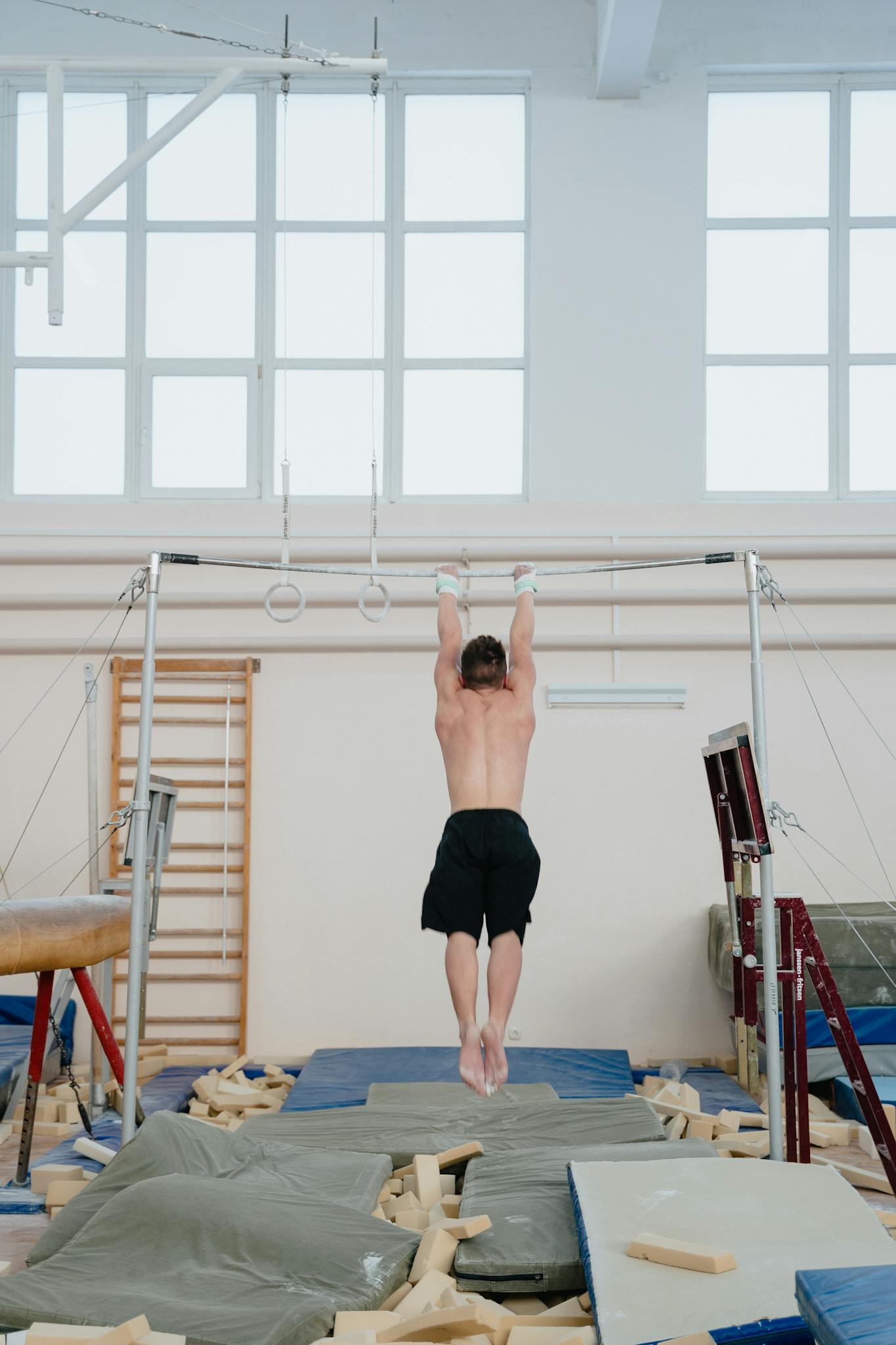 An adult male gymnast practices on gymnastic rings in a gym with safety mats.
